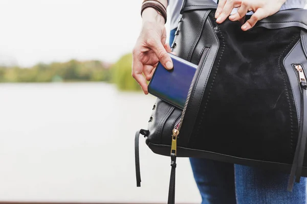 Kot pantolonlu bir kadın, cep telefonunu deri bir çantanın cebinden çıkarıyor. Kot pantolon giymiş bir kadın telefon açmaya çalışıyor.