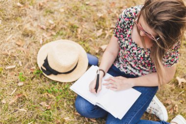 Parkta çimlerin üzerinde otururken kitap yazan güzel bir kadın yazar. Sıradan giyinmiş, gözlüklü bir kadın yazar dışarıda gazetede çalışıyor.