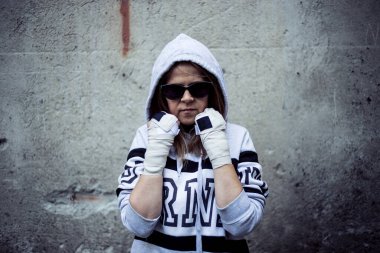 Kadın dövüşçü koruma pozisyonunda. Güneş gözlüğü takan varoş kızı arka planda bir grunge duvarıyla dövüşmeye hazır.