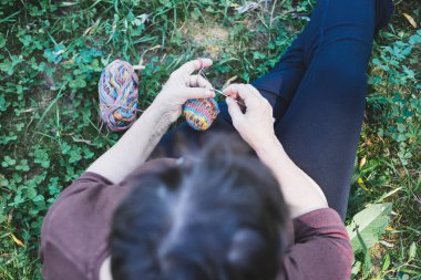 Yeşil çimlerin üzerinde otururken örgü ören yaşlı bir kadın. Yaşlı kadın ince yünden örgü örüyor. Yaşlı dişiler için hoş ve rahatlatıcı bir aktivite.