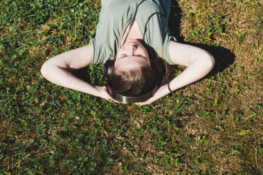 Genç bir kadın bir yaz günü çimlerin üzerinde elleri başının altında yatıyor. Kahverengi saçlı güzel bir kız kulaklıkla müzik dinlerken doğada dinleniyor.