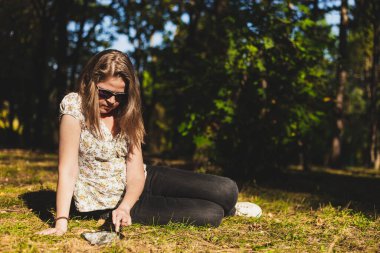 Yan yatarken tablet kullanan bir kadın. Güneş gözlüklü kız yerde otururken mobil cihazdan bir şeyler okuyor.