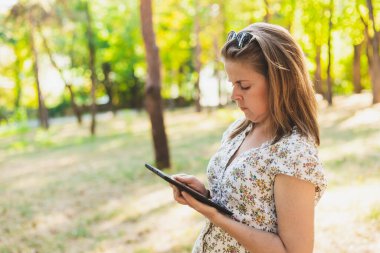 Ormanda tablet kullanan bir kız. Mobil cihazın ekranına dokunan kadın. Uzaktan çalışan profesyonel bir bayan.