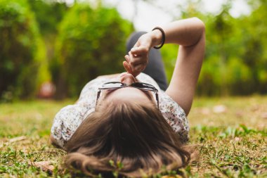 Sırtüstü uzanmış, güneş gözlüğü takmış çivi yiyen gergin bir kadın. Kız tırnaklarını dışarıda yiyor.