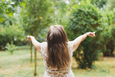 İki elini de havada tutarken genç bir kadının temiz hava almasına dik bir bakış açısı. Kahverengi saçlı güzel kız parkta rahatlıyor ve kendini iyi hissediyor. Çevresel bakım için kavramsal görüntü