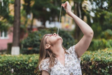 Kız dışarıda sakızıyla oynarken eğleniyor. Sıradan giyinmiş milenyum gözlüğü takıyor ve ağzından beyaz bir sakız çıkarıyor.