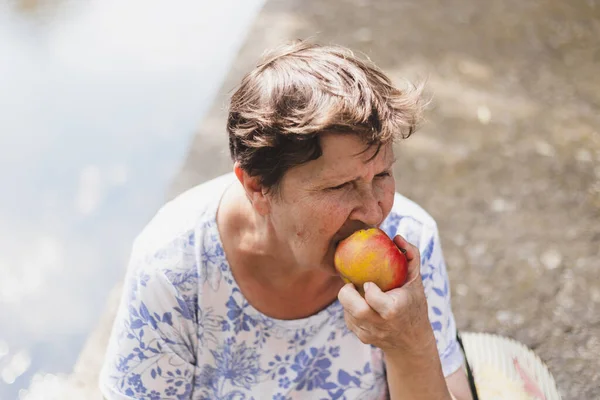 Senior eating apple outside. Portrait of a grandmother sitting and enjoying a nutritious fruit as snack