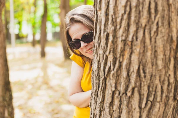 森や公園の木の後ろに隠れてサングラスを持つ妄想少女 誰かを疑いながら見ているストレスの女性 — ストック写真