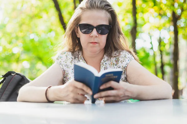 Bible study concept of one young woman with sunglasses. Student studying outside with a small blue book cover in her hands