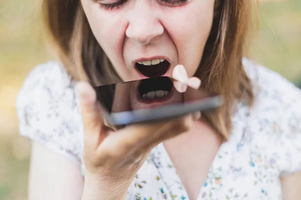 Young woman screaming at her mobile phone outside. Angry girl with brown hair shouting at an unknown call