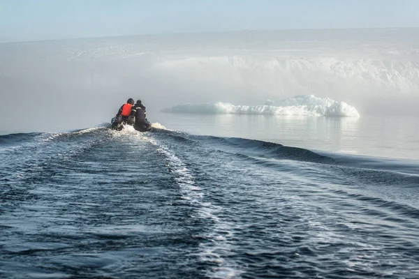 Inflatable boat with people in the waters of the Arctic ocean. Amid the icebergs and the glacier.