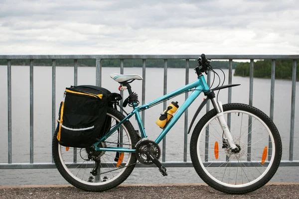 Light-blue all-terrain bicycle with pannier bags and yellow bottle standing infront of lake — Stock Photo, Image