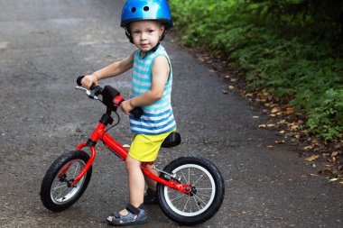 Parlak elbiseli ve kasklı dengeli bisikletli küçük çocuk.