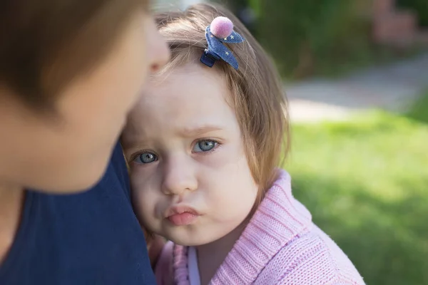 Niña molesta con los ojos azules abrazada por su madre, vistiendo una camiseta azul — Foto de Stock