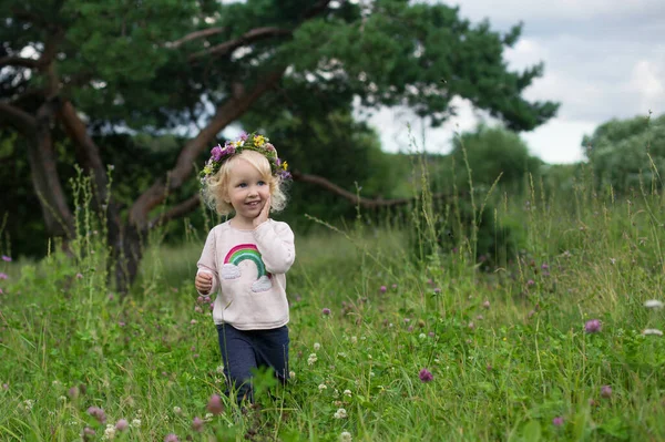 可爱的小女孩 满脸笑容 金发卷曲 头戴野花花环 带着彩虹刺绣和牛仔裤在乡间散步 快乐的夏天和无忧无虑的童年 — 图库照片