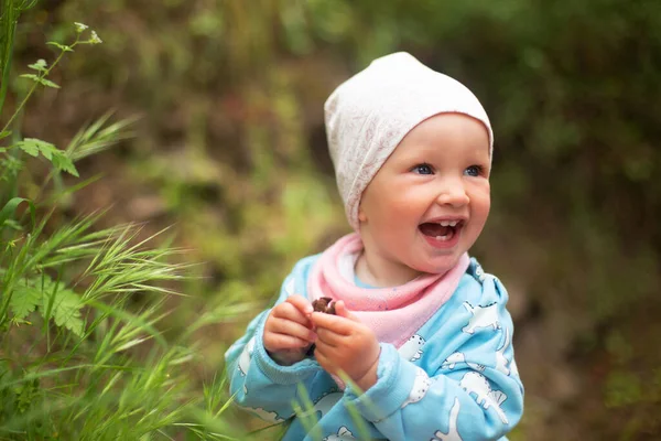 Bébé fille souriante heureuse portant une veste bleu clair et un chapeau blanc debout dehors — Photo