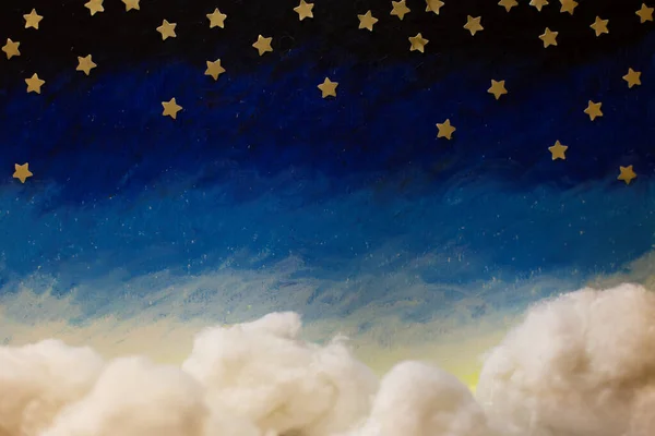 Cartoon painted night sky with bright paper stars and cotton handmade clouds. Blue white gradient
