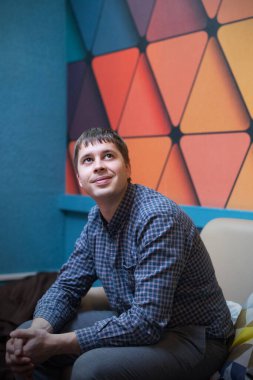 Ekose gömlekli, parlak geometrik duvarlı genç bir adamın portresi.