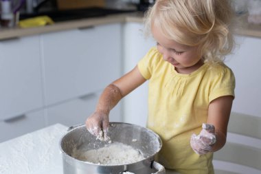 Bebek yemek yapmayı öğreniyor. Sarışın, kıvırcık saçlı, mutfakta hamur yapan küçük tatlı kız..