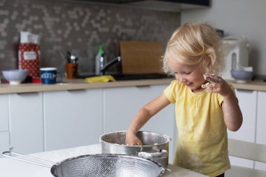 Sarışın, kıvırcık saçlı, mutfakta hamur yapan küçük tatlı kız. Bebek yemek yapmayı öğreniyor.