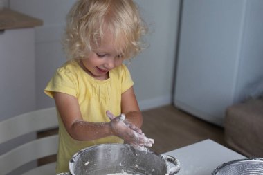 Sarışın, kıvırcık saçlı, mutfakta hamur yapan küçük tatlı kız. Bebek yemek yapmayı öğreniyor.