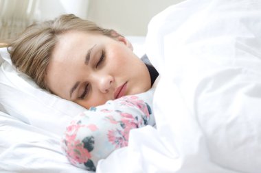 Genç, güzel sarışın kadın beyaz çarşaflarla yatakta uyuyor.