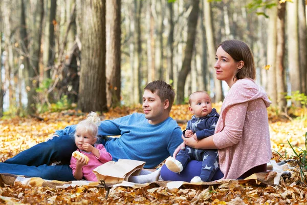 秋の公園で2人の子供を持つ家族 彼らは遊んで軽食を食べて座っている 天気は暖かくて晴れ 黄色の葉が地面に横たわっています — ストック写真