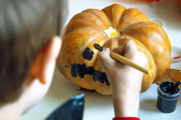 Little boy paints the pumpkin. Close up. Children decorate the house for holiday. Celebrating at home concept.