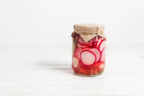 Pickled radish and garlic in a glass jaron on a light background with copy space — Stock Photo, Image