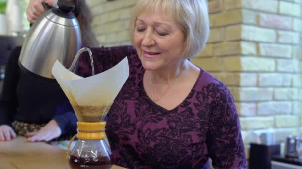 Abuelita-barista vierte agua caliente dentro de la jarra con café — Vídeos de Stock