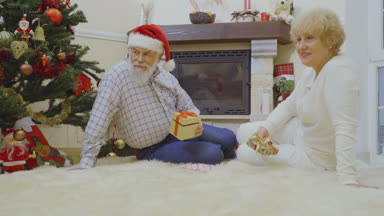 Yaşlı kadın ve adam tüylü halı üzerinde yalan ve Noel hediyeleri değişimi. Mutlu çift çok mutlu ve birbirleri ile birlikte konuşma. Olgun insanlar kış tatil evde geçirmek.