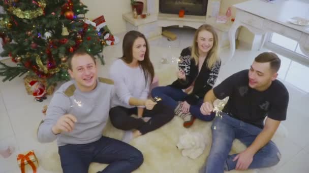 Vier Freunde sitzen mit Wunderkerzen auf dem Boden und feiern Weihnachten — Stockvideo