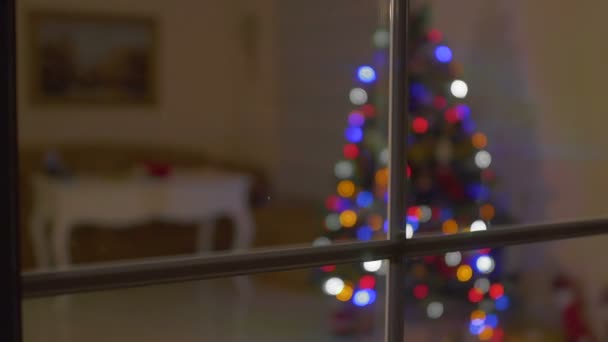 Árvore de Natal está iluminando na sala através da janela no quarto escuro — Vídeo de Stock