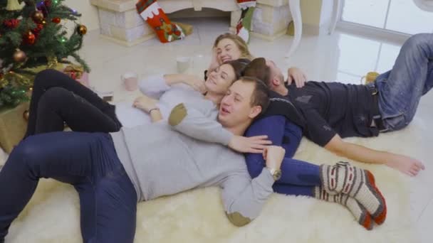 Четверо молодых друзей отдыхают на полу возле елки — стоковое видео