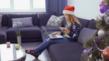 Noel Baba şapkası genç güzel kadın evde koltukta oturur ve online alışveriş yapar.
