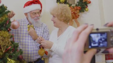 Mutlu çiftimiz Noel ağacı Yılbaşı önce süsleyin. Kadın çift fotoğraf çekmek. Olgun insanlar christams oyuncaklar Noel ağacı ve gülümseyen asmak. Üst düzey insanlar, theie tatil birlikte geçirmek