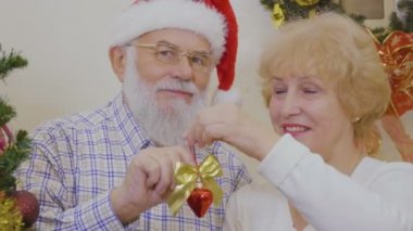 Yaşlı çift oyuncaklar Noel ağacı üzerinde dur. Yaşlı kadın ve adam Noel dekorasyon yapmak için mutlu. Güzel Olgun çift portresi kutlamak Noel evde birlikte.