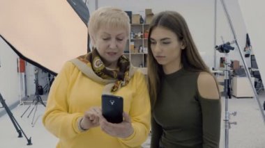 Kadınlar Smartphone'da fotoğraflara bak. İki fotoğrafçılar Fotoğraf yaptıktan sonra atış kompozisyonu tartışmak. Photostudio çalışmalarında profesyonel tasarımcılar.