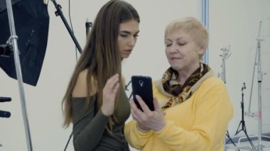 Kadınlar Smartphone'da fotoğraflara bak. İki fotoğrafçılar Fotoğraf yaptıktan sonra atış kompozisyonu tartışmak. Photostudio çalışmalarında profesyonel tasarımcılar.