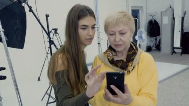 Kadınlar Smartphone'da fotoğraflara bak. İki fotoğrafçılar Fotoğraf yaptıktan sonra atış kompozisyonu tartışmak. Photostudio çalışmalarında profesyonel tasarımcılar.