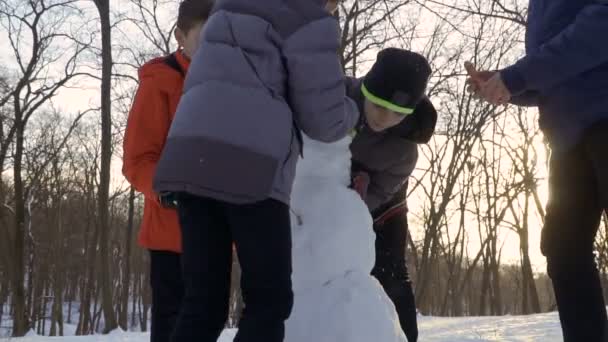 Четыре мальчика делают снеговика в зимнем парке в замедленной съемке — стоковое видео