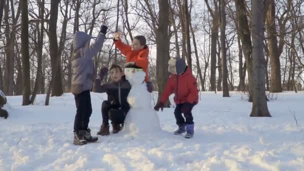 Verspielte Kinder toben in der Nähe eines Schneemanns im Winterpark miteinander — Stockvideo