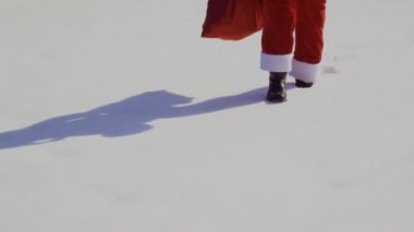Noel Baba kırmızı kostümü içinde kar üzerinde yürüyor. Kar bir sürü.