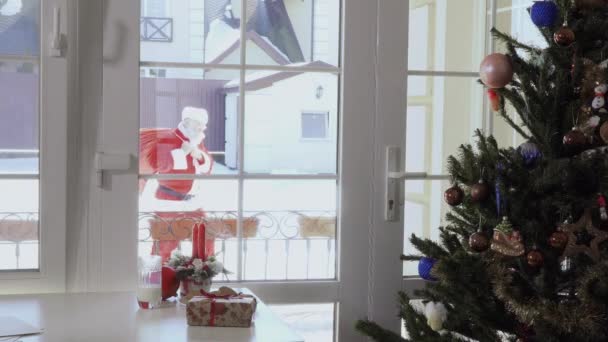 圣诞老人带着红包的礼物走到家里 外面是许多白色和美丽的雪 — 图库视频影像