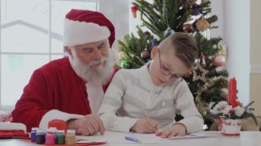 Gözlük ve soyulmuş ceket Santa kucağına oturan küçük çocuk. Çocuk resim veya yazma gümüş pan ile çizer. Yaşlı adam çok dikkatle izliyor ve gülümsüyor. Çocuk çok sıkı çalışıyor ve