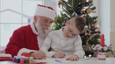 Gözlük ve soyulmuş ceket Santa kucağına oturan küçük çocuk. Çocuk resim veya yazma gümüş pan ile çizer. Yaşlı adam çok dikkatle izliyor ve gülümsüyor. Çocuk çok sıkı çalışıyor ve