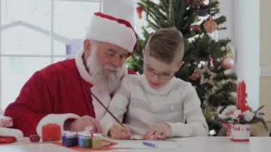 Gözlük ve soyulmuş ceket Santa kucağına oturan küçük çocuk. Çocuk bir fırça ve boya ile ahşap el yapımı makaleler çizer. Yaşlı adam çok dikkatle izliyor ve gülümsüyor. Çocuk
