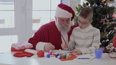 Gözlük ve soyulmuş ceket Santa kucağına oturan küçük çocuk. Çocuk bir fırça ve boya ile ahşap el yapımı makaleler çizer. Yaşlı adam çok dikkatle izliyor ve gülümsüyor. Çocuk