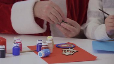 Noel Baba açık yeşil akrilik boya ve çocuk şişeyle şişeye fırça dunk. Çocuk çok renkli noktalar boyar. Masanın üzerine orada şişe bir sürü farklı renkteki kırmızı akrilik boya ile
