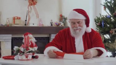 Kırmızı kostümlü parlak bir şekilde dekore edilmiş köknar ağacı ve şömine yakın Noel Baba arıyor nasıl Noel mektupları okur. Yaşlı adam mutlu ve gülümsüyor. Masada iki kırmızı mumlar, küçük Noel baba figürü vardır